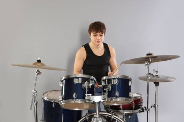 Çubuklu genç çocuk gri arka planda davul çalmayı öğreniyor.