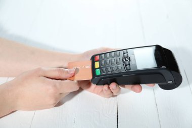 Kredi kartı olan bir kadın beyaz tahta masada ödeme terminalini kullanıyor, yakın plan.