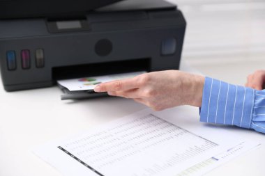 Beyaz masadaki yazıcıdan baskı kağıdı alan kadın, yakın plan.