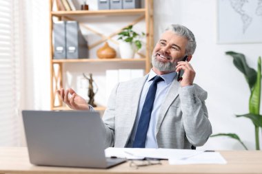 Ofiste akıllı telefonla konuşan takım elbiseli güler yüzlü bir işadamı.