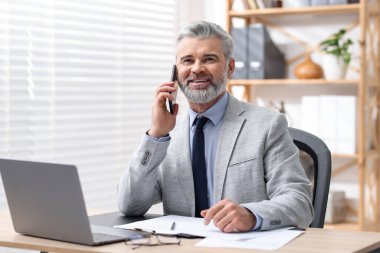 Ofiste akıllı telefonla konuşan takım elbiseli güler yüzlü bir işadamı.