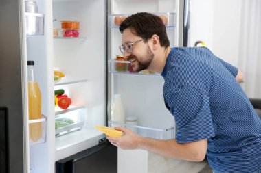 Mutfakta açık buzdolabının yanında peynirli bir adam var.