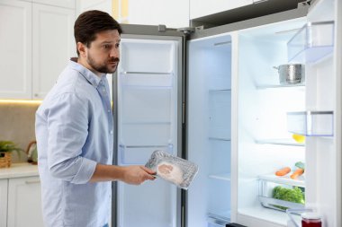 Mutfakta açık buzdolabının yanında çiğ eti olan bir adam.