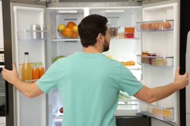 Buzdolabının yanında farklı gıda ürünleri olan bir adam var.