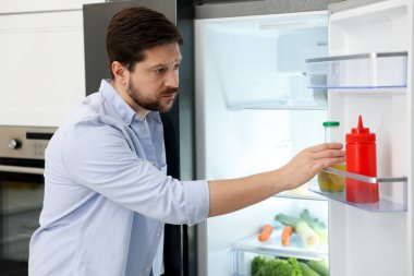 Adam mutfaktaki buzdolabından bir şişe içki alıyor.