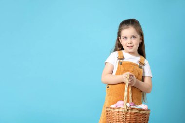 Paskalya kutlaması. Açık mavi arka planda içi yumurta dolu hasır sepeti tutan gülümseyen küçük bir kızın portresi.