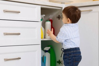 Evde çocuk güvenliği. Küçük çocuk mutfakta temizlik ürünleriyle dolap açıyor.