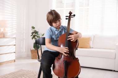 Evdeki sandalyede keman çalan küçük çocuk.