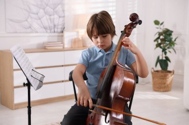 Evdeki sandalyede keman çalan küçük çocuk.