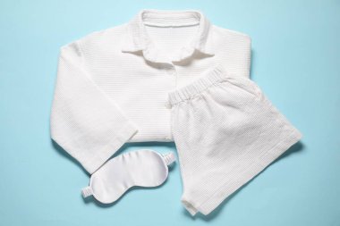 Modaya uygun beyaz pijama ve açık mavi arka planda uyku maskesi.