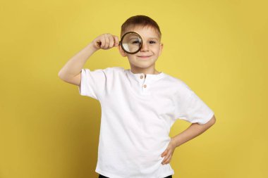 Sarı arka planda büyüteç olan küçük çocuk.