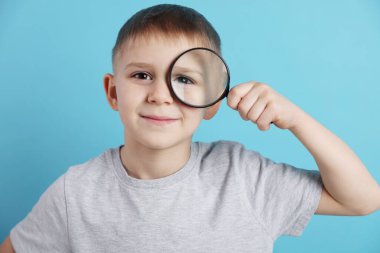 Açık mavi arka planda büyüteç takan küçük çocuk.