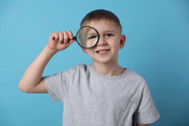 Açık mavi arka planda büyüteç takan küçük çocuk.