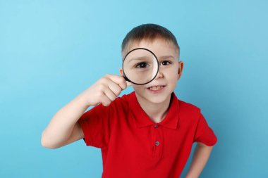 Açık mavi arka planda büyüteç takan küçük çocuk.