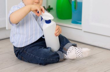 Evde çocuk güvenliği. Küçük çocuk mutfakta temizlik ürünleriyle dolap açıyor.