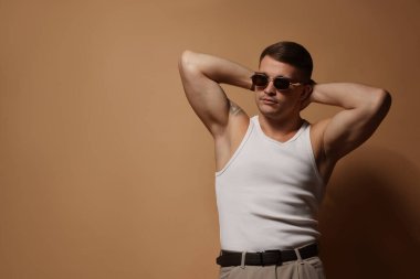 Moda modeli. Bej arkaplanda poz veren güneş gözlüklü yakışıklı adam, metin için boşluk