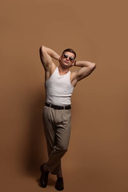 Moda modeli. Güneş gözlüklü yakışıklı adam bej arka planda poz veriyor.