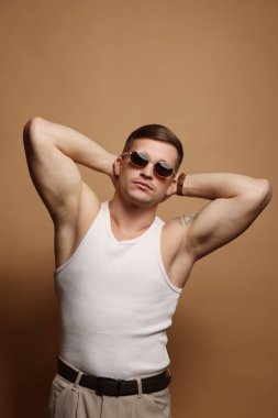 Moda modeli. Güneş gözlüklü yakışıklı adam bej arka planda poz veriyor.