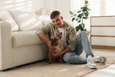 Evdeki kanepenin yanında tatlı köpeğiyle rahatlayan genç bir adam.