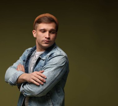 Moda modeli. Koyu yeşil arka planda çapraz kolları olan şapkalı ve ceketli yakışıklı bir adam.