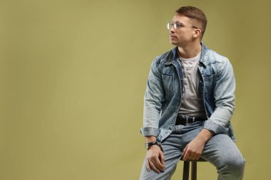 Moda modeli. Yeşil arka planda dışkısı olan gözlüklü ve ceketli yakışıklı bir adam.