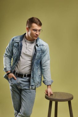 Moda modeli. Yeşil arka planda dışkısı olan gözlüklü ve ceketli yakışıklı bir adam.