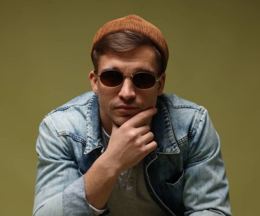 Moda modeli. Şapkalı, güneş gözlüklü ve ceketli yakışıklı bir adam.