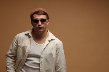 Moda modeli. Bej arka planda şapka ve güneş gözlüklü yakışıklı adam, mesaj için yer