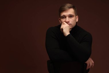 Moda modeli. Koyu kahverengi arka planda poz veren yakışıklı adamın portresi, metin için boşluk