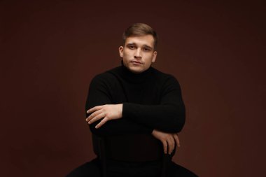 Moda modeli. Koyu kahverengi arka planda poz veren yakışıklı bir adamın portresi.