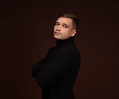 Moda modeli. Koyu kahverengi arka planda poz veren yakışıklı bir adamın portresi.
