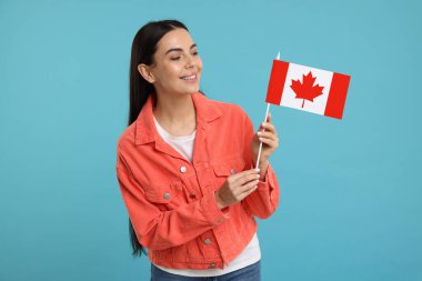 Açık mavi arka planda Kanada bayrağı taşıyan mutlu kadın