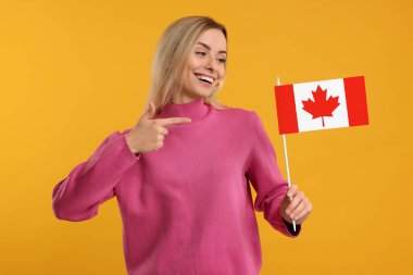 Turuncu arka planda elinde Kanada bayrağını gösteren mutlu kadın.