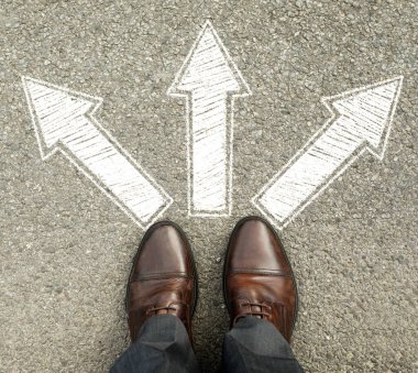 Yolda dikilen, farklı yönlere bakan okları olan ayakkabılı bir adam. Yolculuğuna başla.