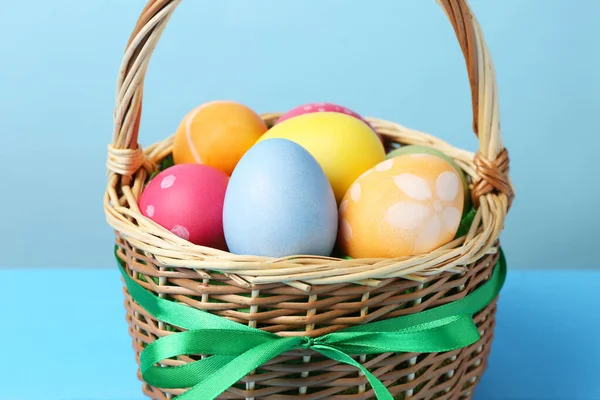 Hasır sepete boyanmış Paskalya yumurtaları açık mavi arkaplanda, yakın plan.