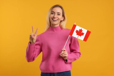 Kanada bayrağı taşıyan mutlu kadın turuncu arka planda barış jesti gösteriyor
