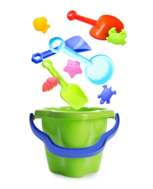 Çocuklar için plaj oyuncakları. Plastik kum kalıpları ve aletler beyaz arkaplanda kovaya düşüyor