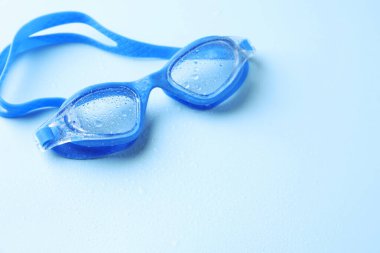 Açık mavi arka planda su damlaları olan yüzme gözlükleri, yakın plan. Metin için boşluk