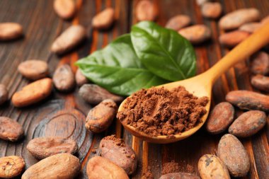 Doğal kakao çekirdekleri, toz ve yeşil yapraklar ahşap masada, yakın plan.