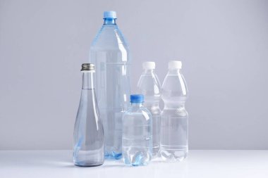 Beyaz masada gri arka planda farklı boyutlarda su şişeleri