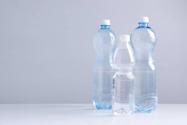 Beyaz masada gri arkaplan ile farklı boyutlarda su şişeleri, metin için boşluk