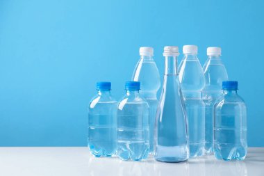 Beyaz masada açık mavi arka planda farklı boyutlarda su şişeleri var. Metin için boşluk