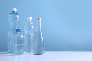 Beyaz masada açık mavi arka planda farklı boyutlarda su şişeleri var. Metin için boşluk