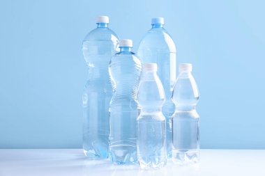 Açık mavi arka planda beyaz masada farklı boyutlarda su şişeleri