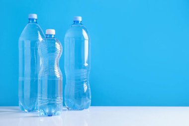 Beyaz masada farklı boyutlarda su şişeleri açık mavi arkaplan, metin için boşluk