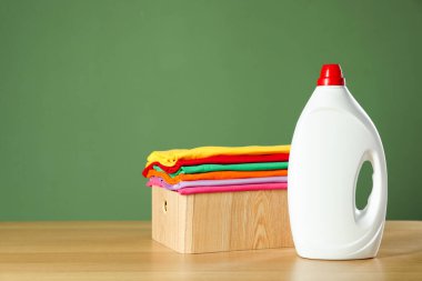 Koyu yeşil arka planda çamaşır sepeti ve ahşap masa üzerinde deterjan, metin için boşluk