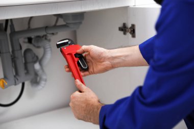 Boruların yanında boru anahtarı olan bir tesisatçı, yakın plan.