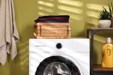 Çamaşır sepetinin içinde çamaşır makinesinin üzerinde katlanmış temiz kıyafetler var.