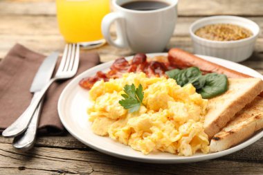 Lezzetli bir kahvaltı. Lezzetli çırpılmış yumurta, domuz pastırması ve sosis, ahşap masada servis edilir, yakın plan.
