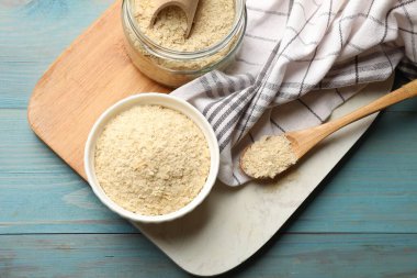 Kasedeki kuru maya taneleri, cam kavanoz, kaşık ve kepçe açık mavi ahşap masa, üst manzara